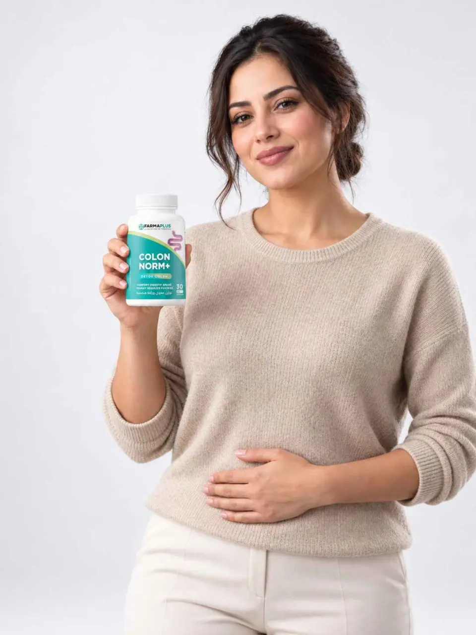 Femme souriante tenant le flacon de Colon Norm+ par FARMAPLUS, la main posée sur le ventre, sur fond gris clair
